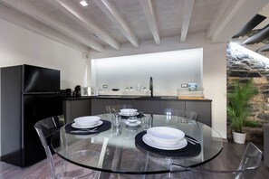 A modern kitchen with a glass dining table, black appliances, and a stone accent wall. - Blue Diamond Suite (Como)