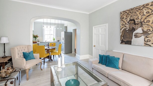 A living room with a sofa, armchair, and glass coffee table. There is a dining area with yellow chairs and a table. A kitchen is visible in the background. - Fabulous 2 bedroom garden apartment very close to town centre (Bath)