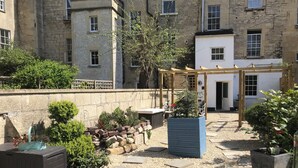 A courtyard with a wooden pergola, potted plants, a brick wall, and a stone building in the background. - Fabulous 2 bedroom garden apartment very close to town centre (Bath)