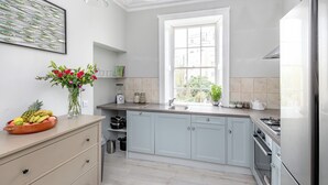 A modern kitchen with light blue cabinets, a stainless steel refrigerator, and a window providing natural light. - Fabulous 2 bedroom garden apartment very close to town centre (Bath)