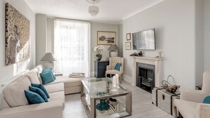 A living room with a sofa, a glass coffee table, a fireplace, and a television on the wall. - Fabulous 2 bedroom garden apartment very close to town centre (Bath)