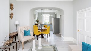A modern living room with a sofa, a glass coffee table, and a dining area with yellow chairs. - Fabulous 2 bedroom garden apartment very close to town centre (Bath)