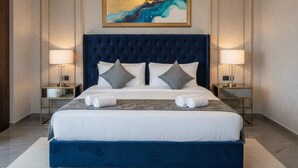 A king-sized bed with a dark blue upholstered headboard, two bedside tables with lamps, and a large abstract painting above the bed. - Hotel Grande Villa Near Delhi Airport (New Delhi)