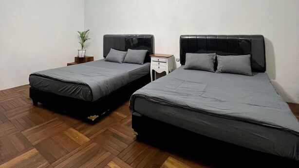 A room with two beds, a wooden herringbone floor, a ceiling light fixture, and a small bedside table with a plant. - Lovia Villa Dieng (Kejajar)