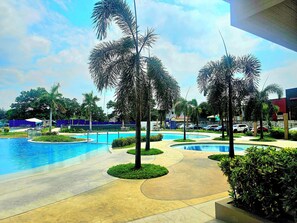 Un área de piscina con varias piscinas, palmeras y un paseo pavimentado.