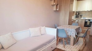 Una habitación pequeña y acogedora con sofá, una mesa con sillas y una zona de kitchenette.