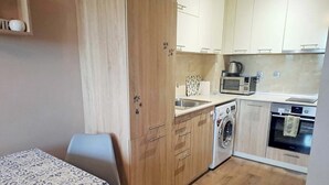 Una cocina compacta con armarios de madera, lavadora, microondas y pileta.