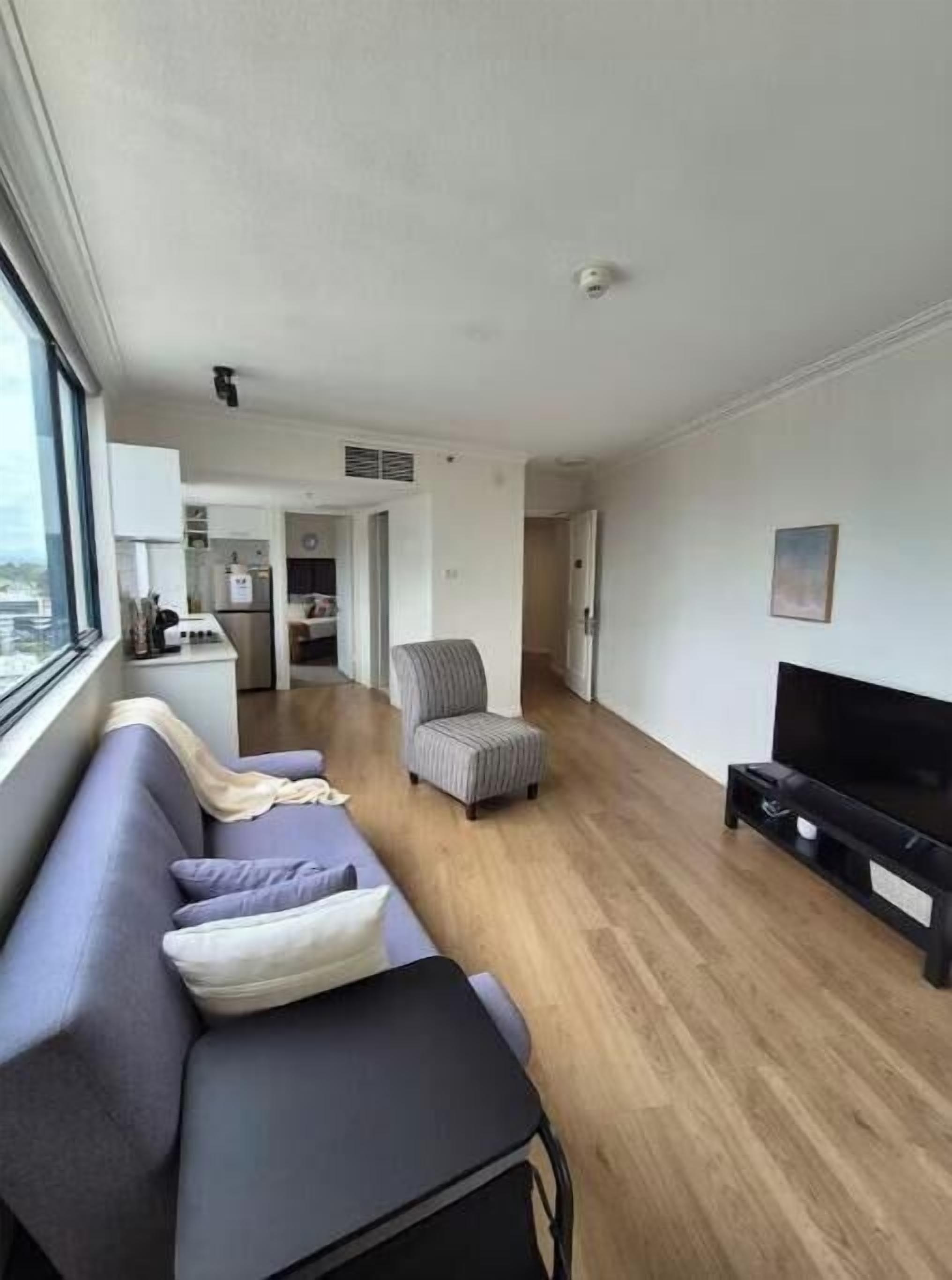 A modern living room with a sofa, a television, and a kitchen in the background.