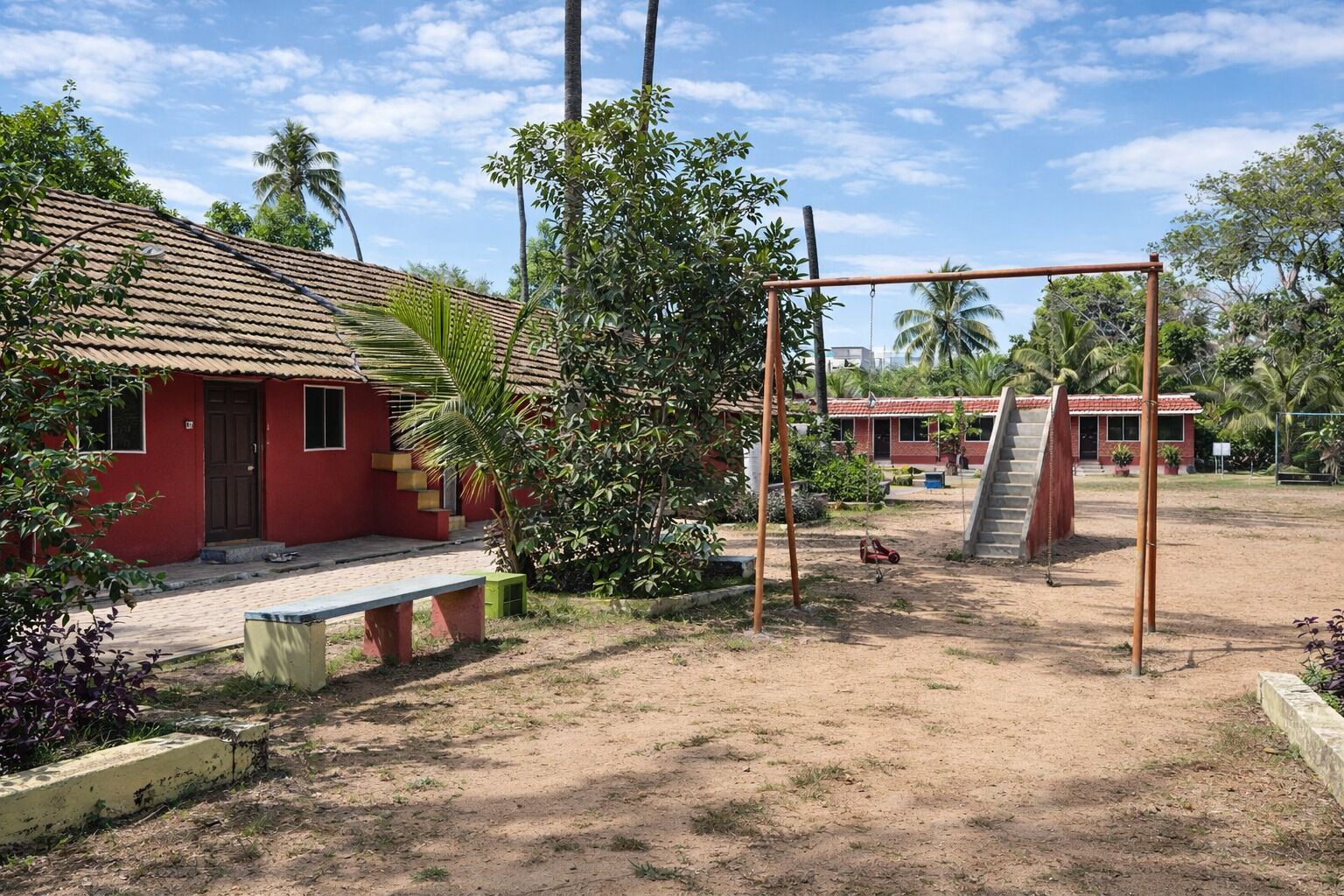 A red building with a tiled roof, a swing set, and a dirt ground.