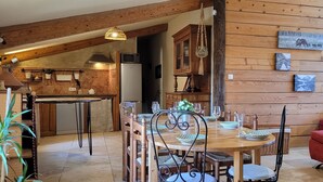 A cozy kitchen with wooden walls, a dining table set with chairs, and a red sofa in the living area. - La Bergerie d'Hélène (Salles-sous-Bois)