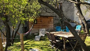 A wooden deck with a table and chairs, surrounded by trees and a stone wall. - La Bergerie d'Hélène (Salles-sous-Bois)