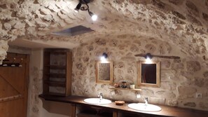 Een eenvoudige badkamer met stenen muren, houten planken en twee wastafels met spiegels.