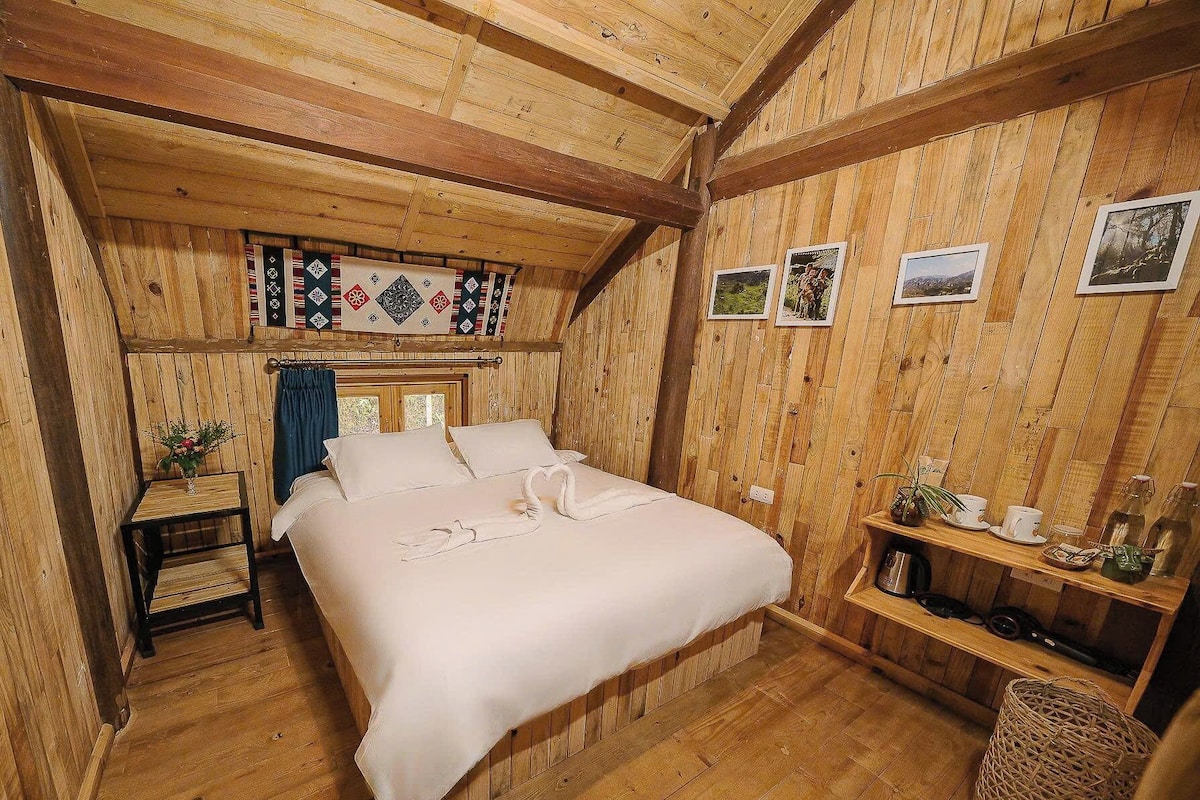 Una camera accogliente in legno, con un letto, un tavolino con un vaso e una mensola con vari oggetti.