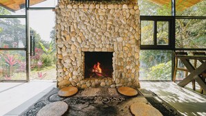 A stone fireplace with a fire, surrounded by a wooden bench and a woven rug. - TV Palm Ecolodge Ha Giang (Ha Giang 1)