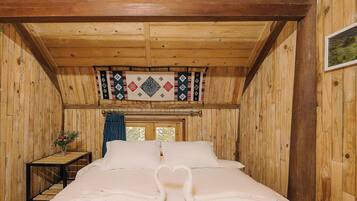 A wooden cabin room with a bed, a small table with a vase, and a window with curtains.