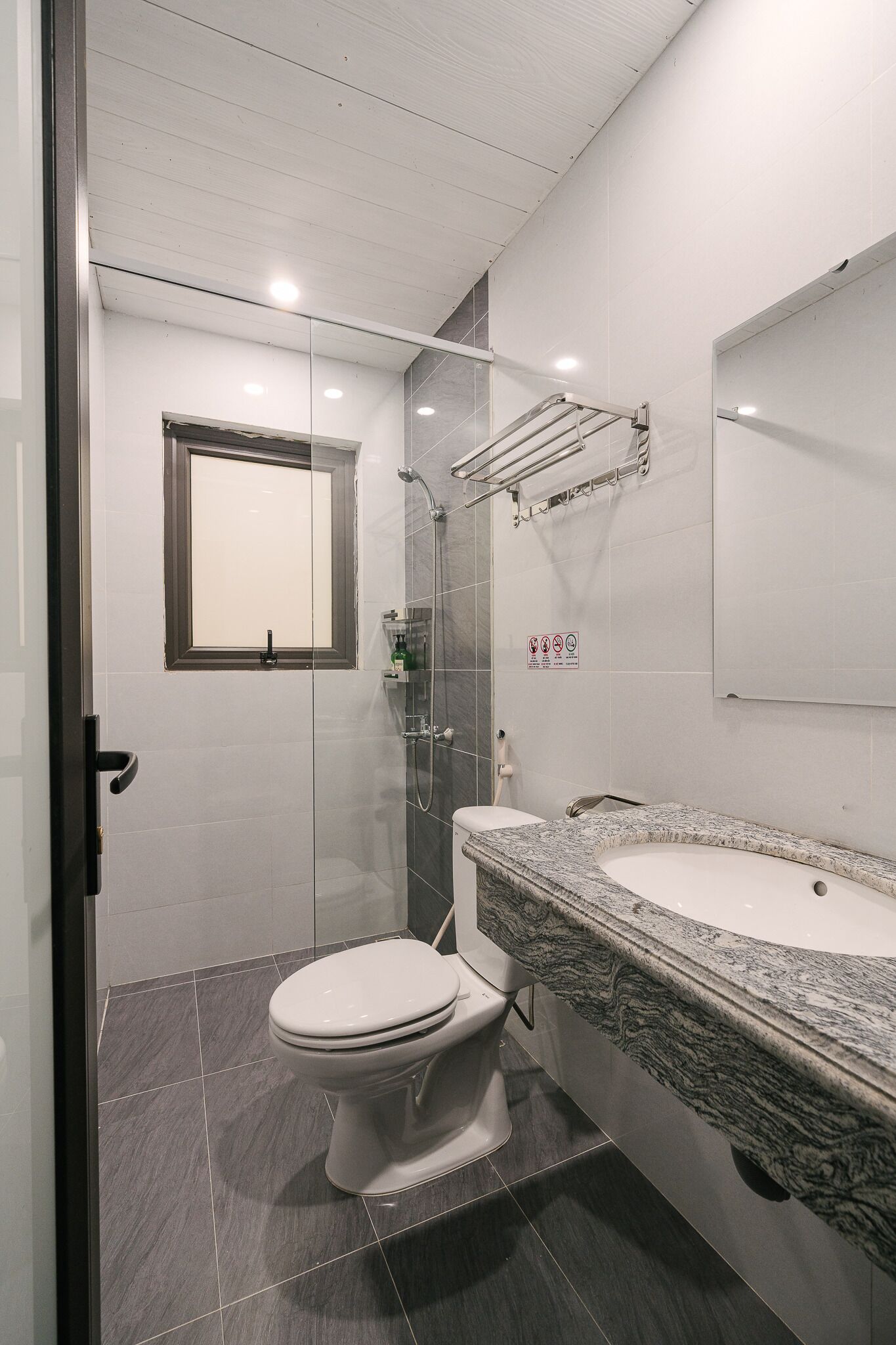 A modern bathroom with a glass-enclosed shower, a white toilet, and a granite countertop sink.