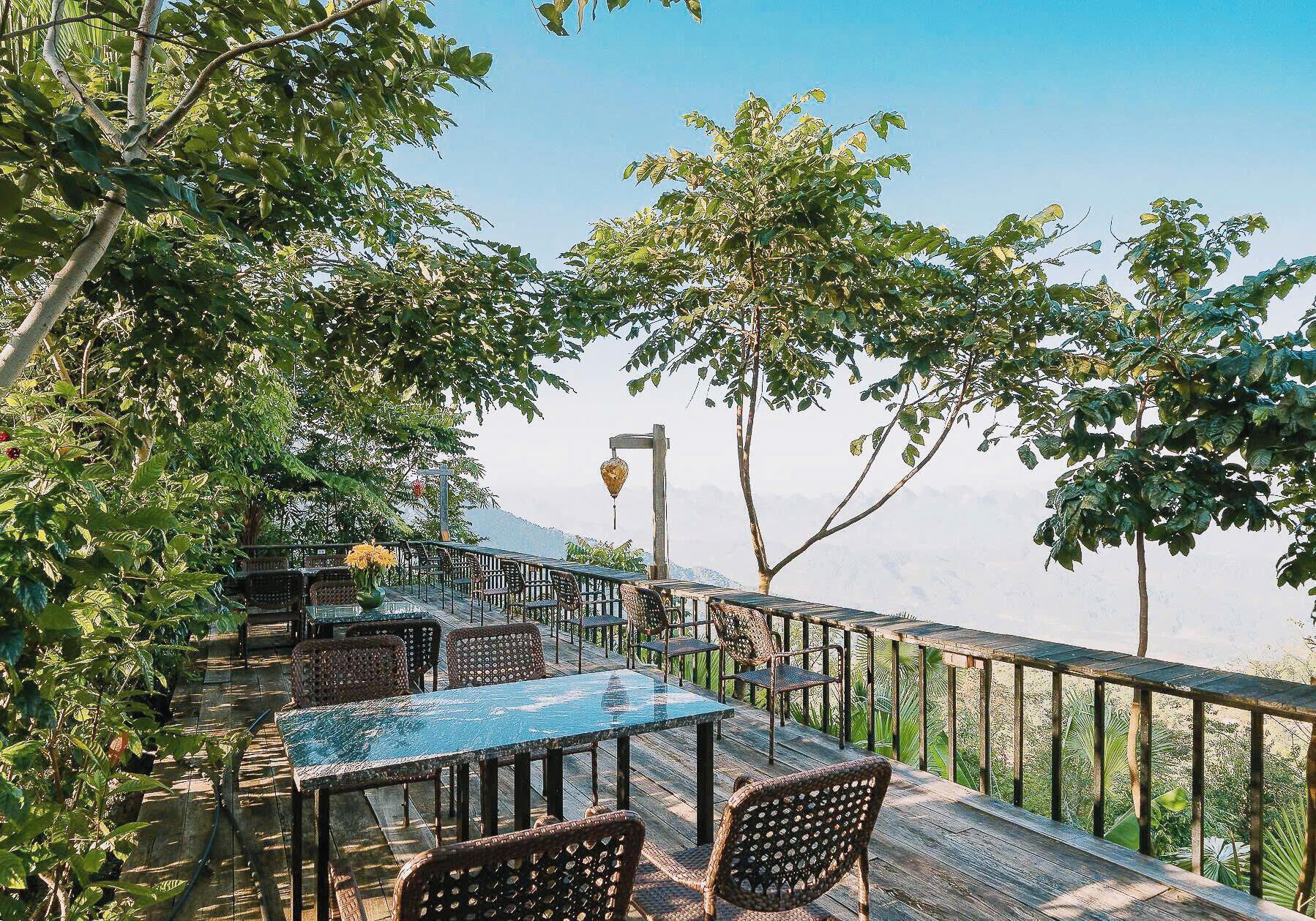 An outdoor dining area with tables and chairs, surrounded by trees and a view of the landscape.