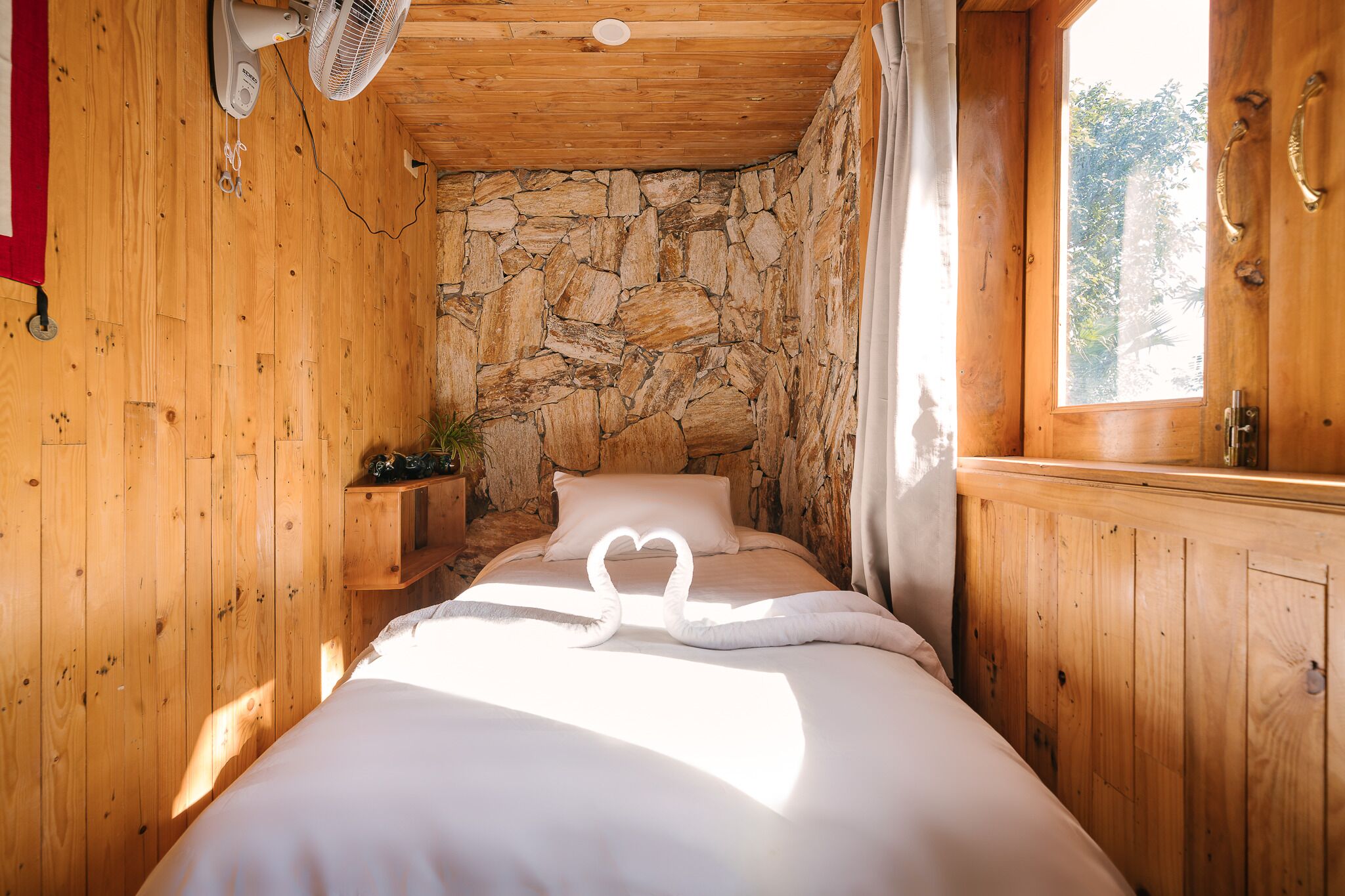 Una stanza accogliente in legno, con un muro in pietra, un letto con lenzuola bianche e una ventola a soffitto.