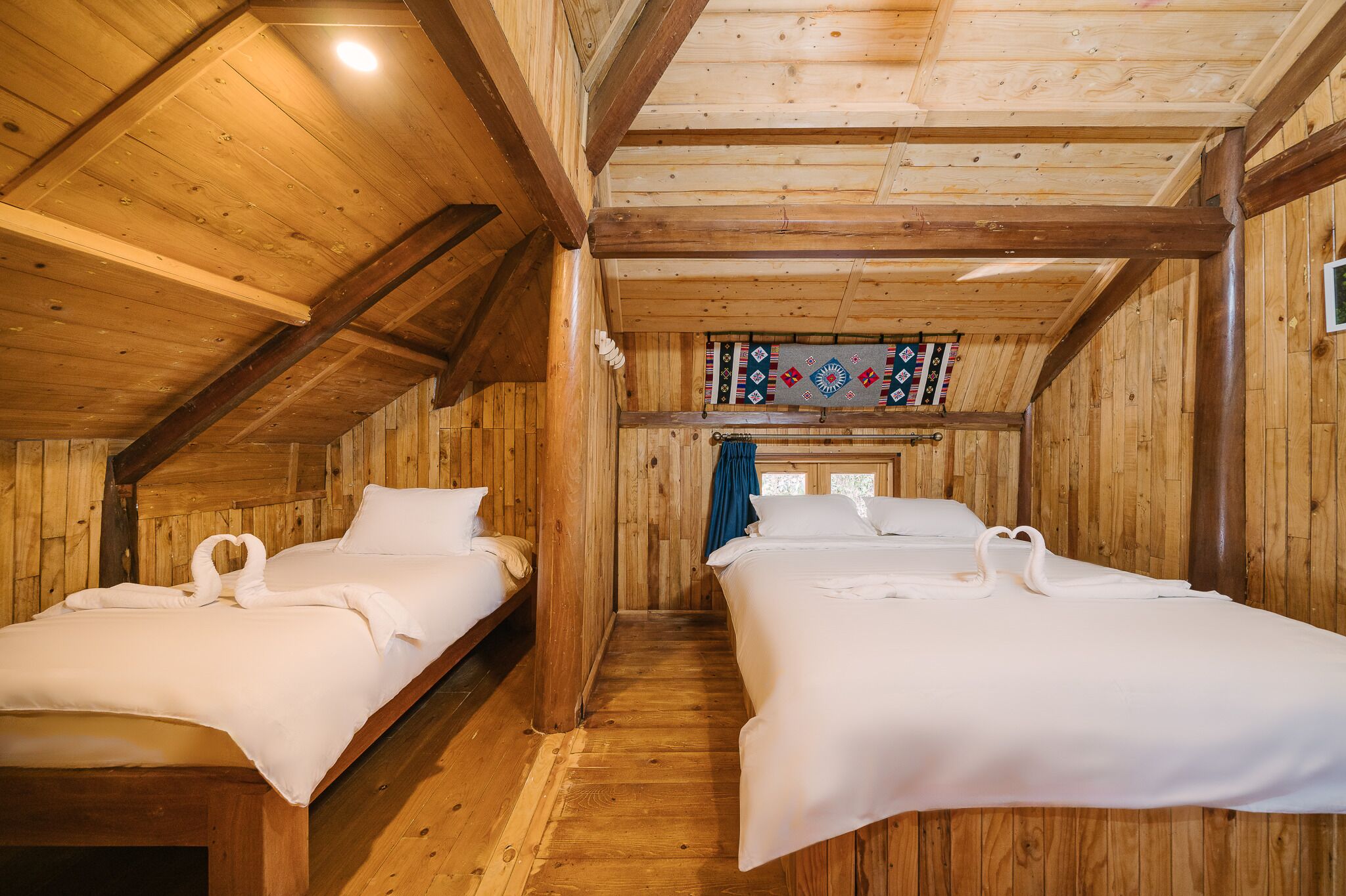 A wooden cabin with two beds, a wooden ceiling, and a stained glass window.