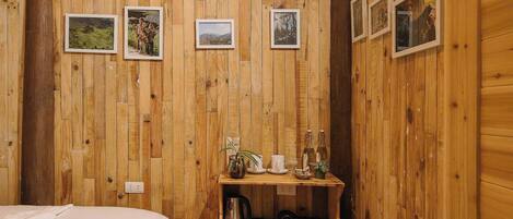 Quarto de cabana de madeira com uma cama, uma prateleira com objetos e três quadros na parede.