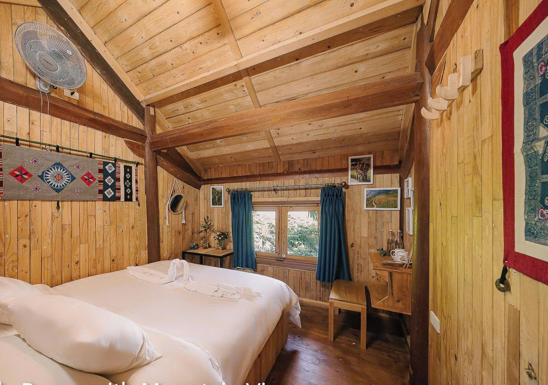 Quarto de cabana de madeira com cama, escrivaninha e janela com cortinas.