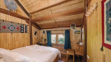 Quarto de cabana de madeira com cama, escrivaninha e janela com cortinas.