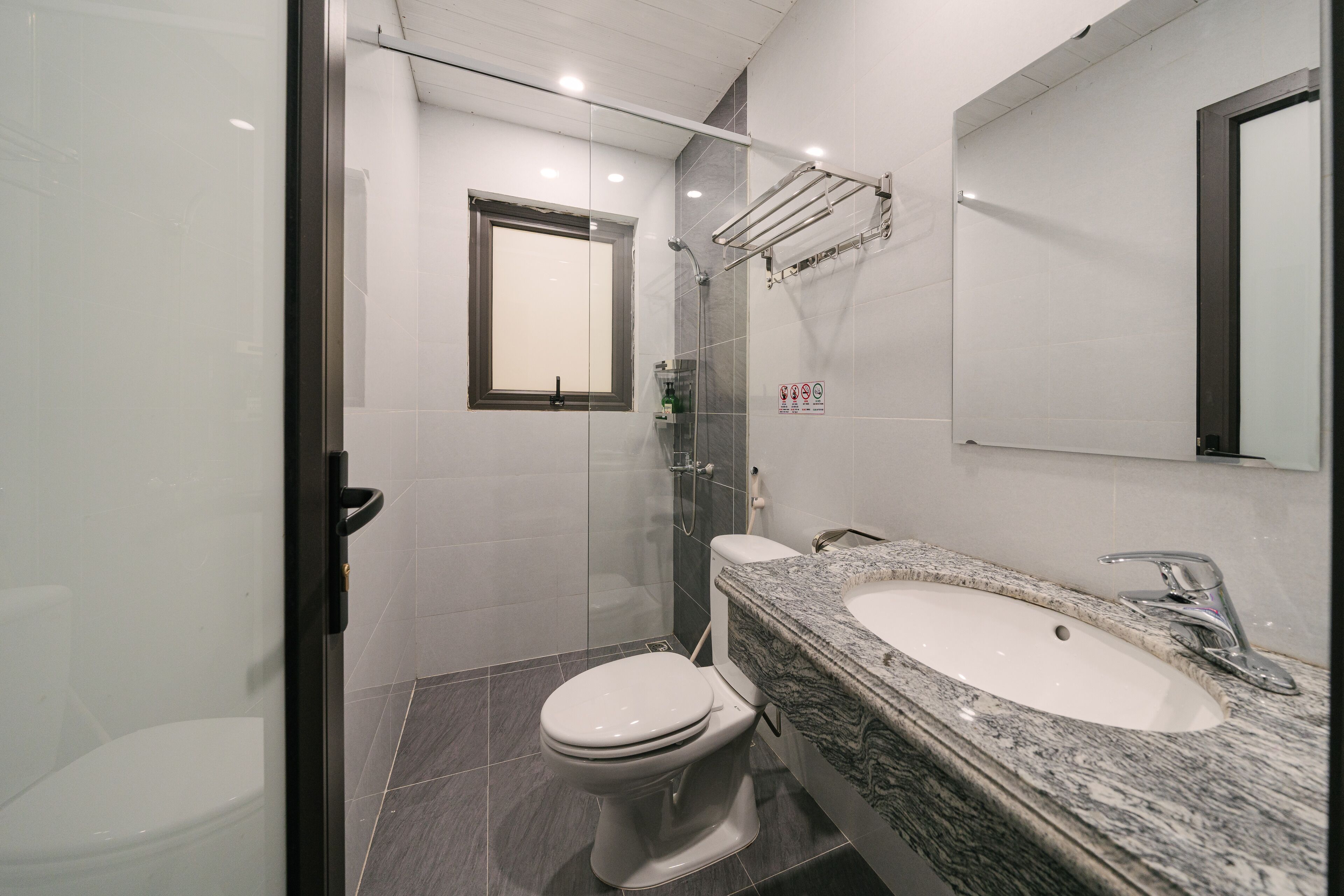 A modern bathroom with a glass-enclosed shower, a white toilet, and a granite countertop sink.