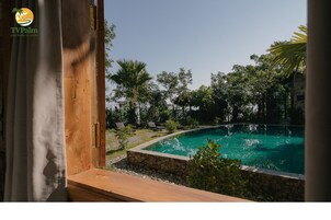 A view of a swimming pool surrounded by greenery, with a wooden deck and stone walls.