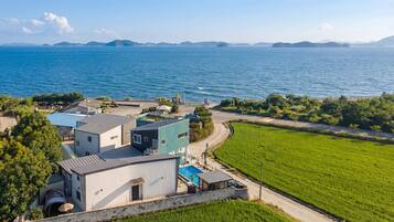 A coastal property with a swimming pool, a tennis court, and a view of the sea.