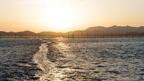 A calm body of water with a visible wake, surrounded by a fence and distant mountains under a clear sky.