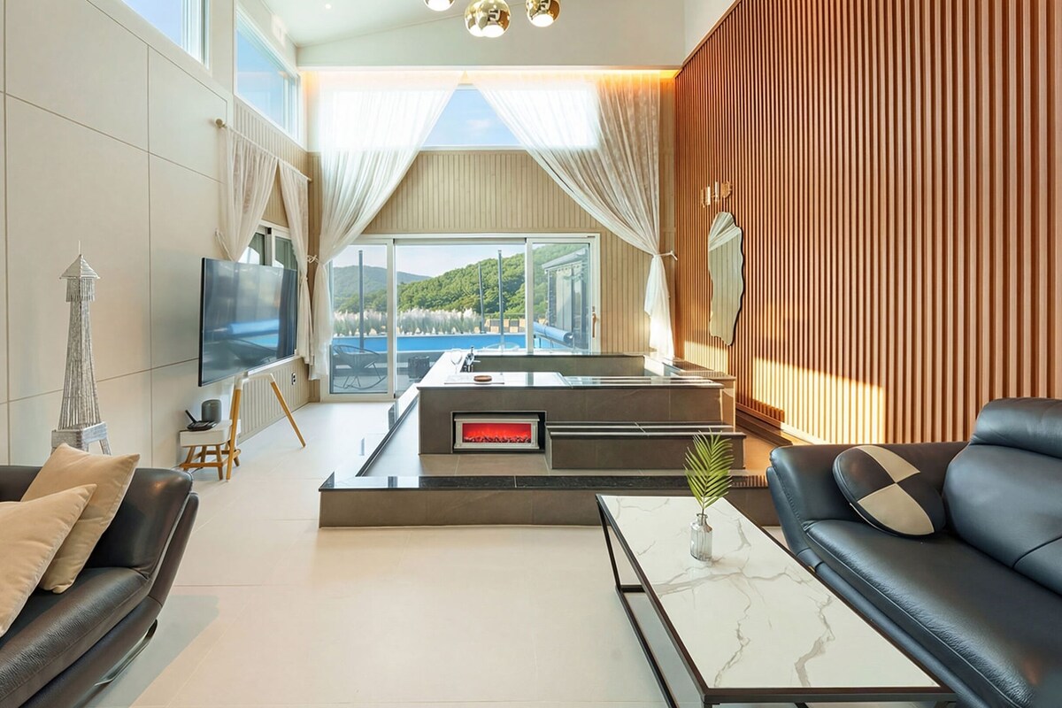 Ein modernes Wohnzimmer mit Fernseher, Ledersofas, einem Marmortisch und Seeblick.