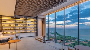 A modern interior with a large window overlooking a coastal view, a built-in bookshelf, and a seating area with a view. - Sea View Luxury -  Experience The Exclusivity (Muang Pattaya)