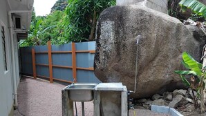 Un lavandino in cemento con un tubo, una roccia grande e una recinzione metallica in un'area giardino.