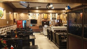 A restaurant with wooden decor, a Coca-Cola fridge, and a counter with a TV. - Fauzi Rasoi & Guest House (Faizabad)