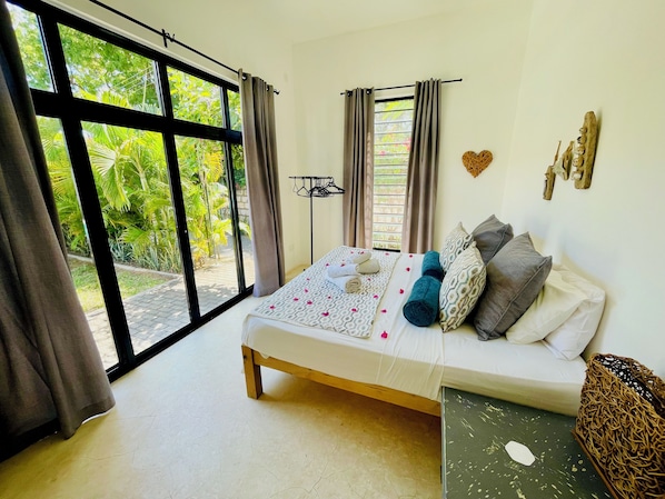 Een slaapkamer met een bed, gordijnen, uitzicht op groen en een wandrek.