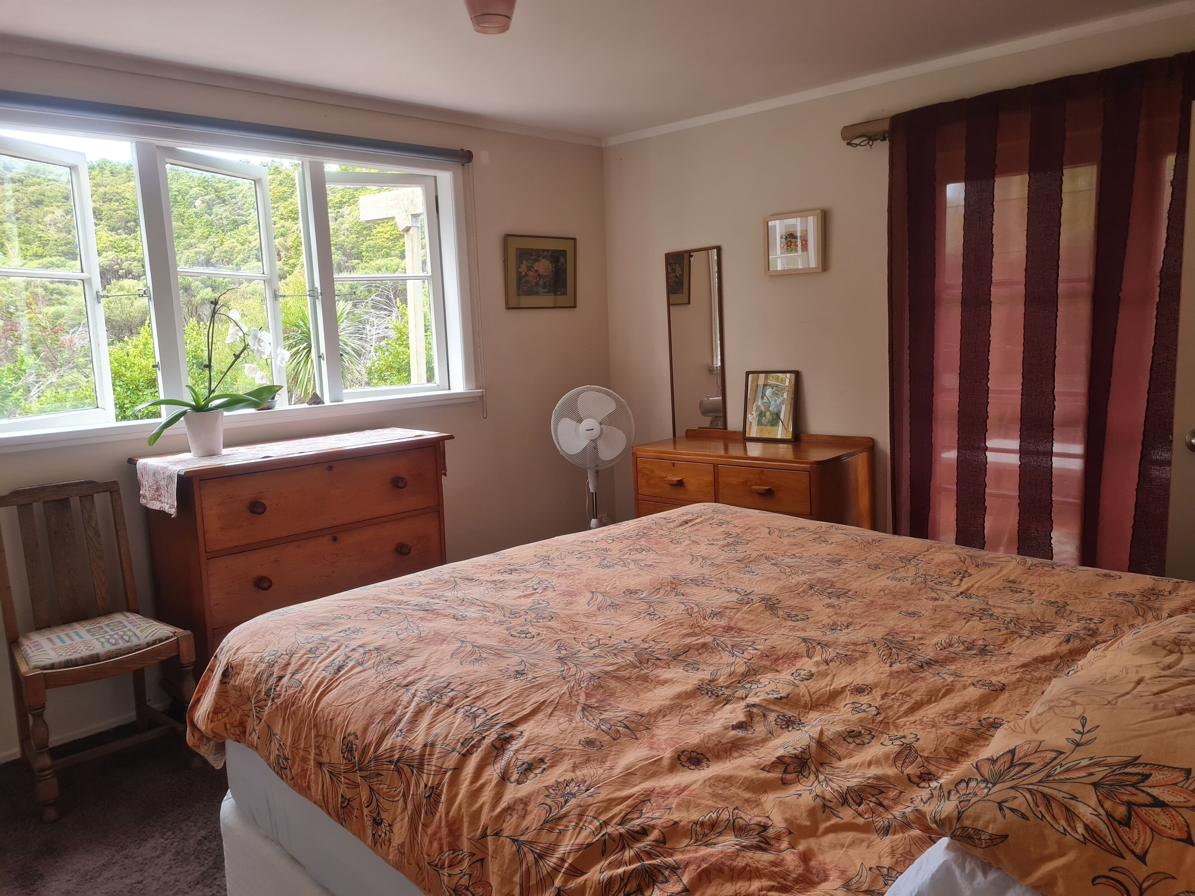 A bedroom with a bed, dresser, chair, and a window with a plant.