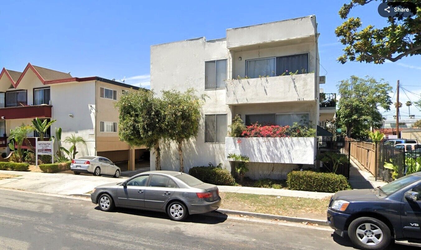 A two-story residential building with a balcony on the second floor, a parked car in front, and a street view.