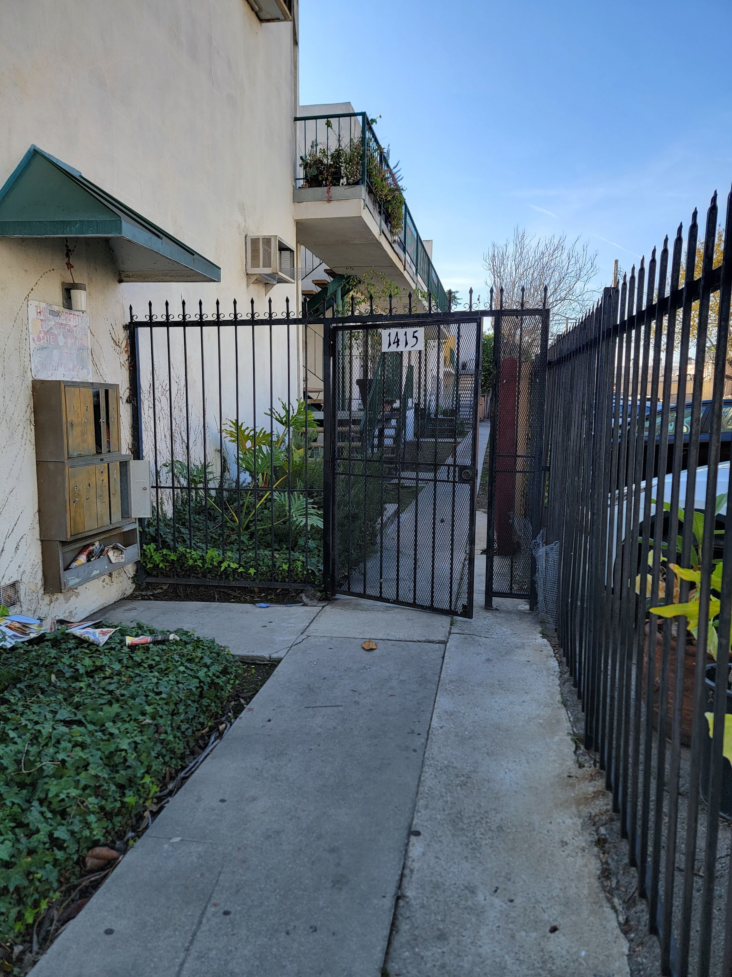 Zona residencial cerrada con un camino de hormigón, una puerta metálica con un número y un edificio con toldo verde.