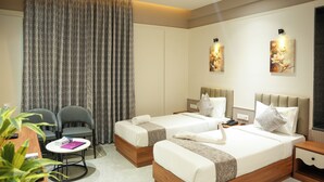 Une chambre d’hôtel avec deux lits, un bureau avec une chaise, une petite table et une grande fenêtre avec des rideaux.
