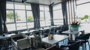 Un restaurant avec des tables, des chaises, un ventilateur de plafond et de grandes fenêtres avec des rideaux.