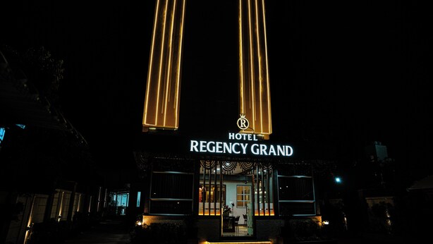La façade du Regency Grand Hotel la nuit, avec ses colonnes verticales illuminées et son panneau indicateur bien visible.