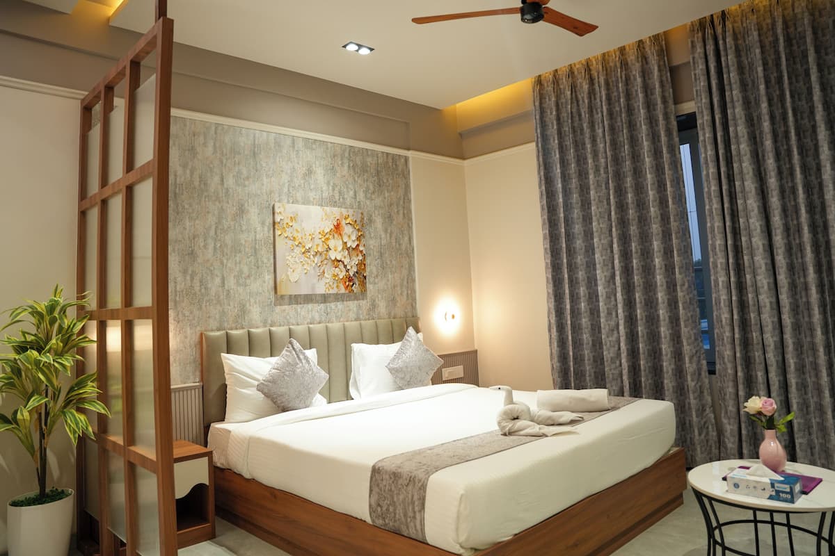 A modern hotel room with a large bed, a ceiling fan, a wall-mounted light, a potted plant, and a view of the outdoors through the window.