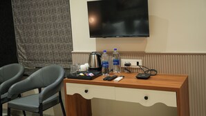 Une chambre d’hôtel avec un bureau en bois, deux chaises grises, un téléviseur à écran plat et un mini-bar.
