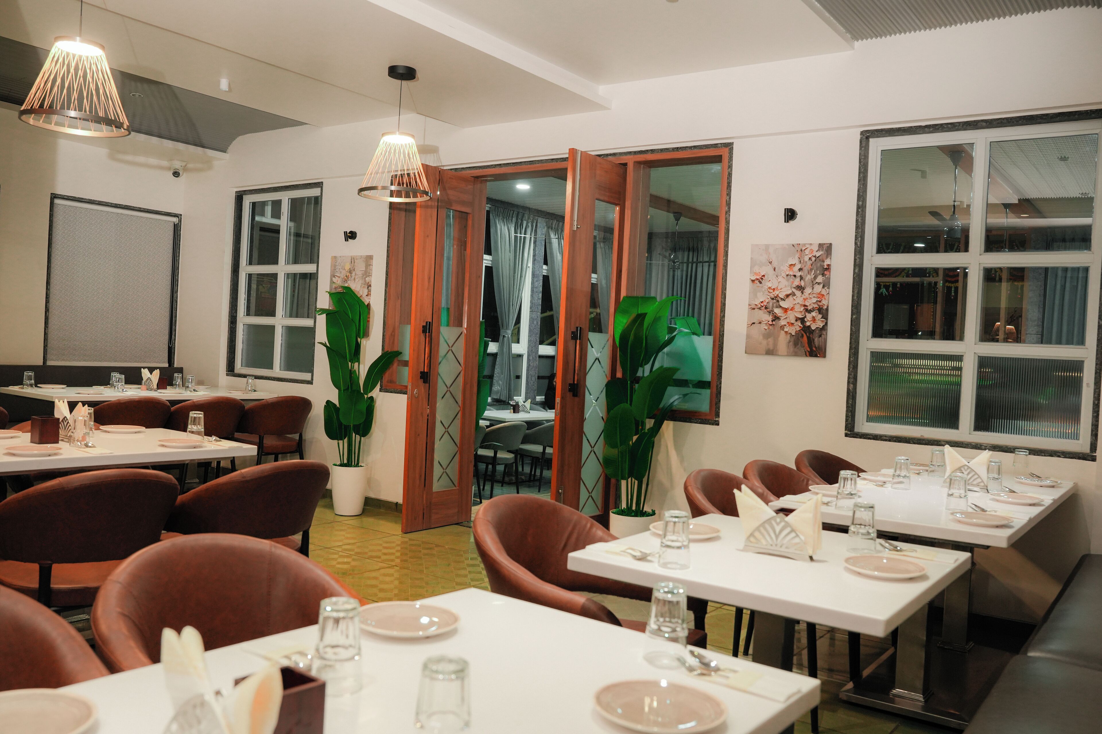A dining area with tables set for four, chairs, and potted plants.