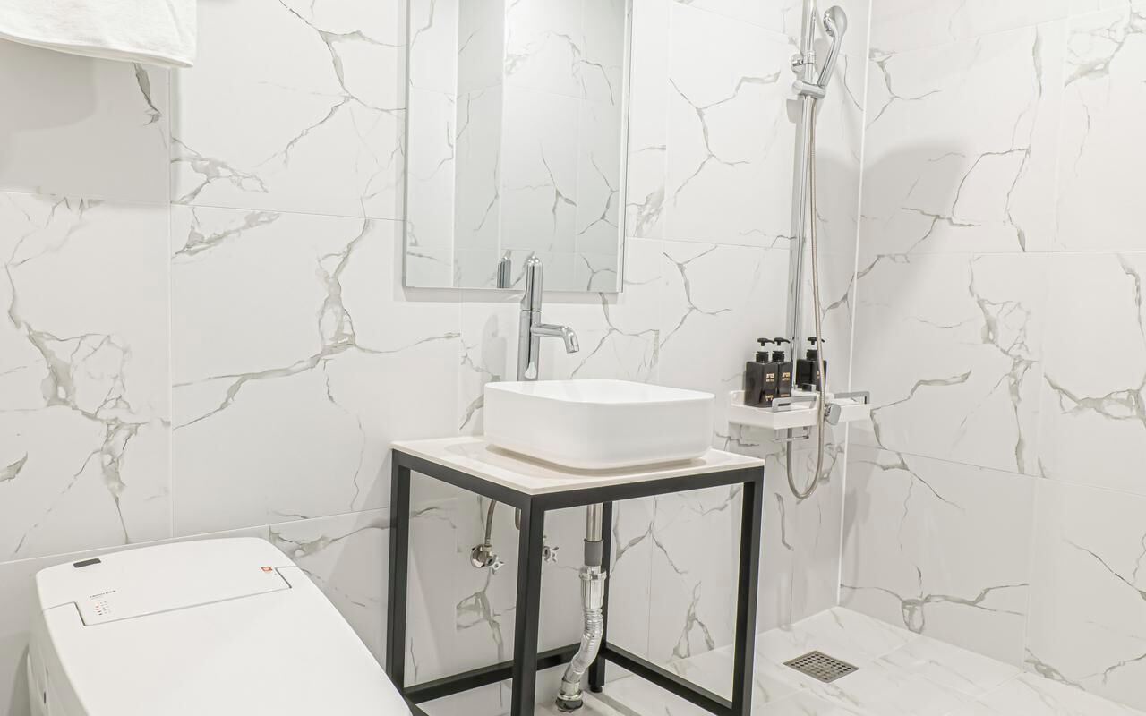 Un baño con lavamanos blanco, espejo y ducha.