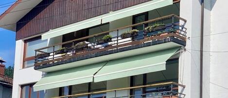 A multi-story building with balconies, a visible entrance, and a street view.