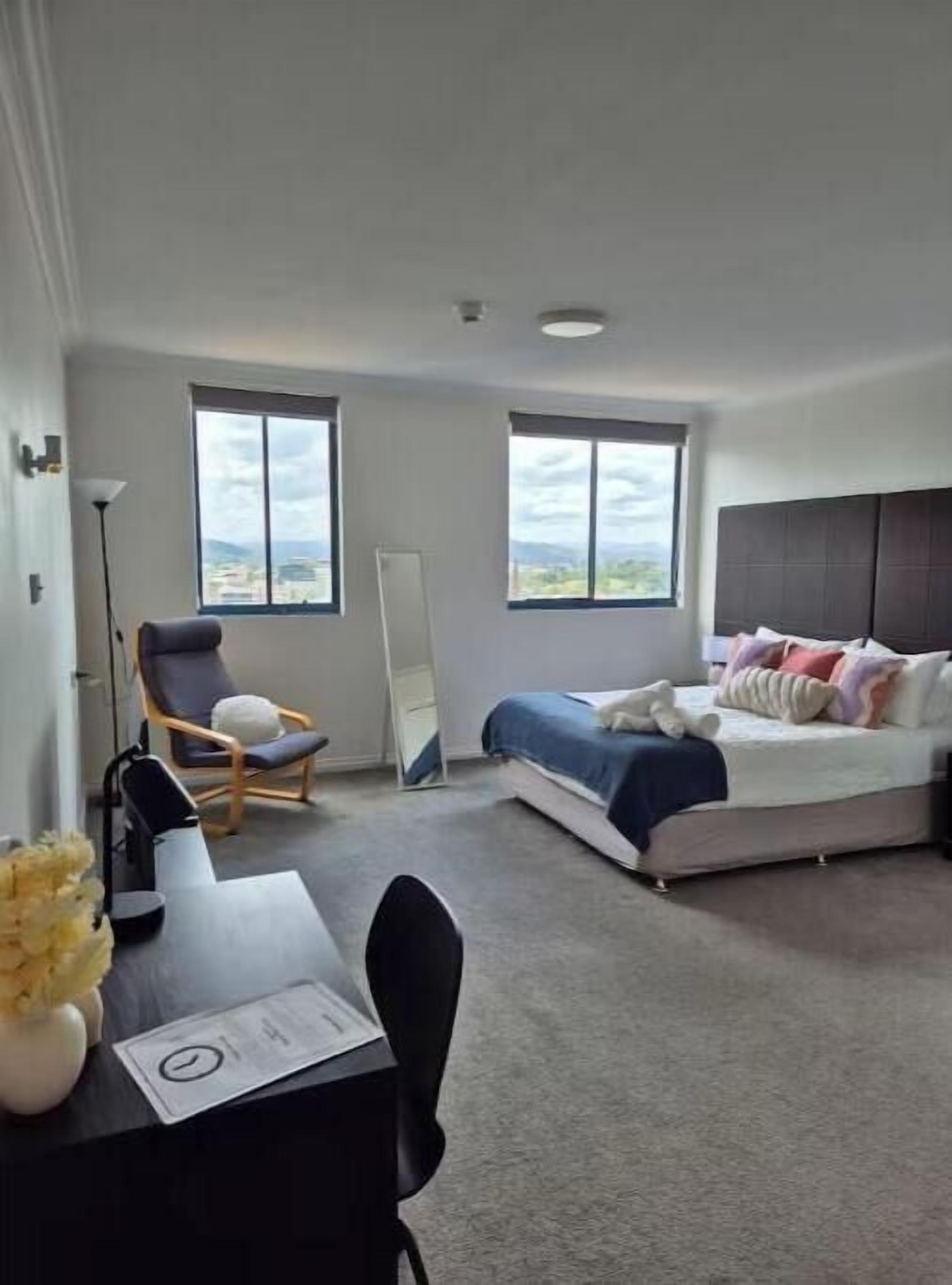 A bedroom with a bed, a chair, a desk, and a large window.