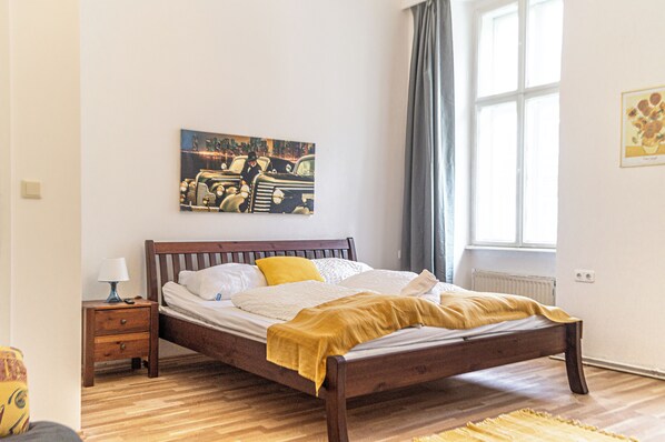 A bedroom with a wooden bed, a nightstand, a lamp, a painting on the wall, and a window with curtains. - Near Wiener Stadthalle - 4BR Apt. w/ WIFI (Vienna)