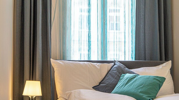 A neatly made bed with pillows, a bedside lamp, and curtains. - Near Wiener Stadthalle - 4BR Apt. w/ WIFI (Vienna)