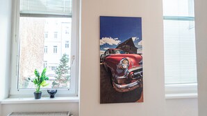 A room with a window, a painting of a vintage car, and a potted plant on the windowsill. - Near Wiener Stadthalle - 4BR Apt. w/ WIFI (Vienna)